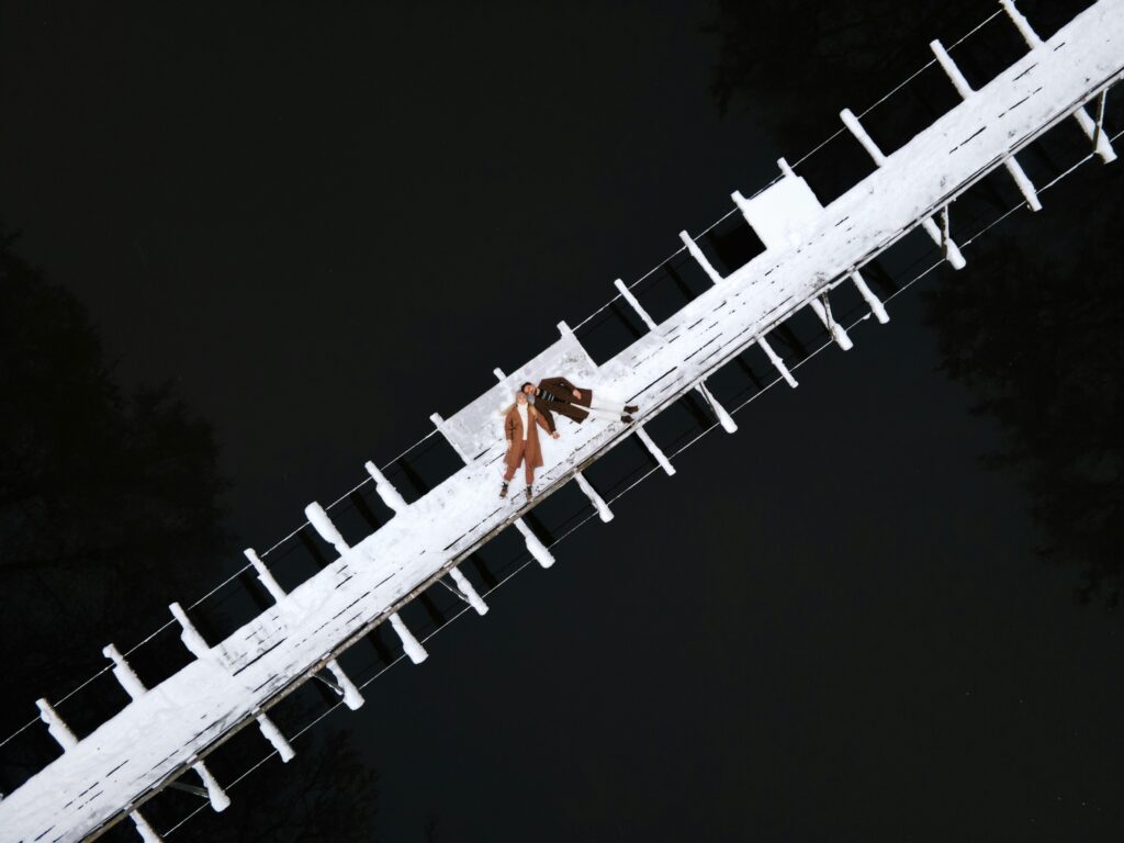 Couple walking hand in hand on a snow-covered pier over a lake, captured from above.